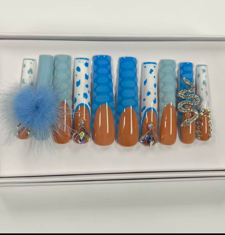 Available at Jazz Beauty Supply in Detroit, this set of decorative false nails features blue, white, and brown designs with geometric patterns, rhinestones, a fuzzy blue pom-pom, and a gold snake embellishment.